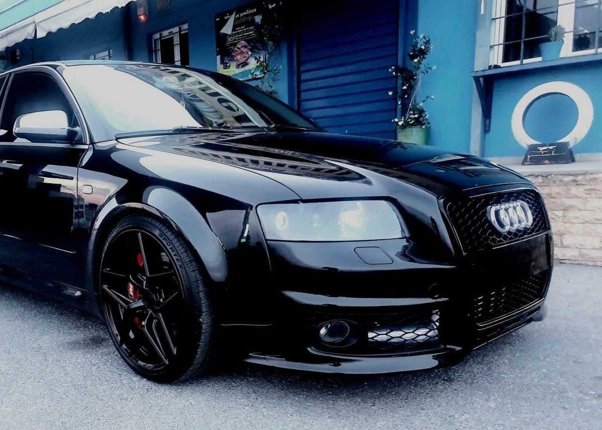 Black Audi sedan with custom front bumper and dark wheels parked in front of blue building